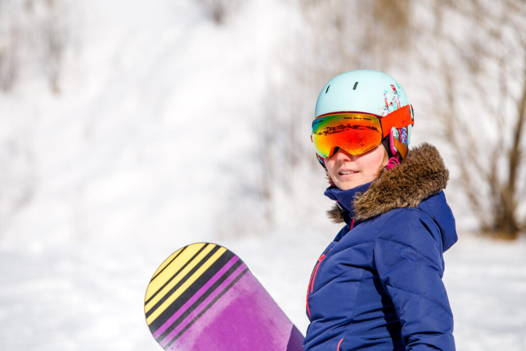 Fetiță pregătită de o sesiune de snowboard, pe pârtie.